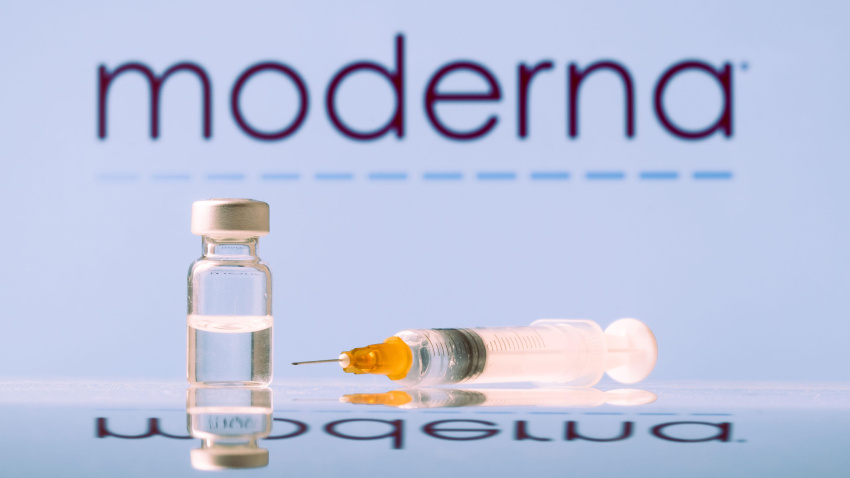 Frasco y jeringa de la vacuna Moderna contra el coronavirus con el logotipo como fondo.