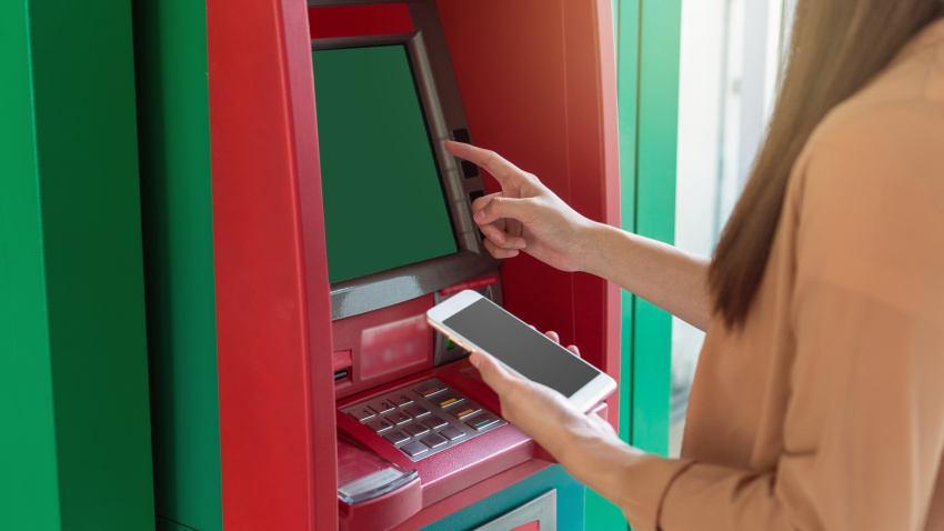 woman using the smart mobile phone for withdrawing in front of the ATM