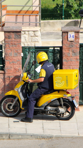Cartero de Correos repartiendo correo desde una moto amarilla en Santander, Cantabria