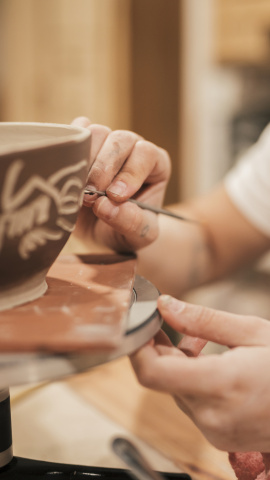 Una artesana decora una pieza de barro moldeada en un torno