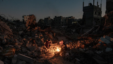 Palestinos sentados junto a un fuego sobre los escombros de su casa destruida en Khan Yunis, en el sur de la Franja de Gaza, el 20 de octubre de 2024