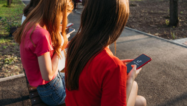 Tres chicas conversan con sus teléfonos inteligentes en el parque. Amigas de la generación Z que usan dispositivos y se divierten al aire libre