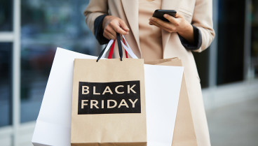 Mid-section portrait of stylish young woman holding shopping bags with Black Friday and texting on the go while leaving mall in sale season, copy space