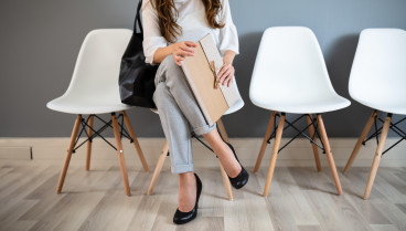 Joven empresaria sosteniendo una carpeta mientras está sentada en una silla esperando una entrevista de trabajo