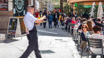 Un camarero sirve bebidas en la terraza de un bar repleto