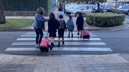 Varios alumnos con sus padres cruzan por un paso de peatones para acudir al colegio