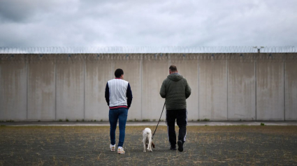 Dos internos de la cárcel de Pamplona pasean en el interior del recinto con uno de los perros. EFE/Cedida