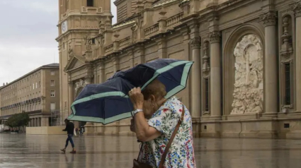 Imagen de archivo de una mujer cruzando la plaza del Pilar bajo la lluvia.