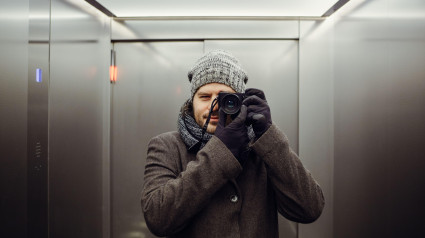 Fotógrafo masculino tomándose una autofoto en un ascensor. Autorretrato frente al espejo, aprendizaje de la fotografía y concepto de apariencia con película analógica