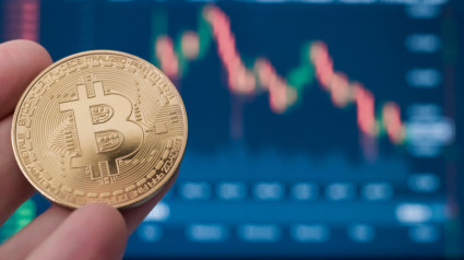 Moneda de criptomoneda Bitcoin acuñada en la mano con una pantalla de operaciones de mercado en el fondo