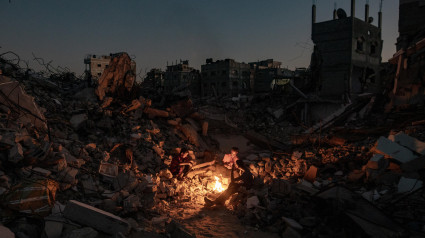 Palestinos sentados junto a un fuego sobre los escombros de su casa destruida en Khan Yunis, en el sur de la Franja de Gaza, el 20 de octubre de 2024