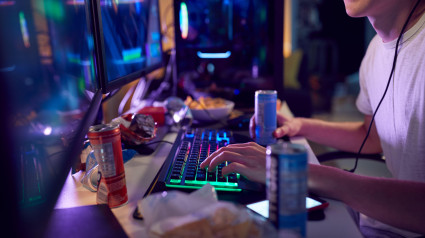 Adolescente bebiendo cafeína mientras juega en casa usando dos pantallas de computadora por la noche