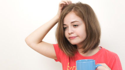 Retrato de una joven caucásica, bostezando, cansada o somnolienta, con el pelo tupido y despeinado, sosteniendo una taza de café