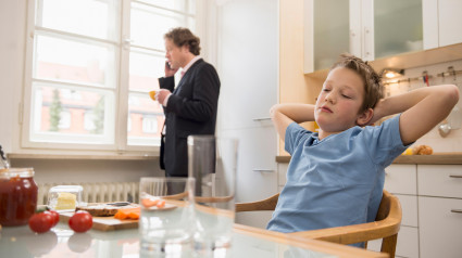 Niño aburrido en la cocina con su padre hablando por teléfono de fondo