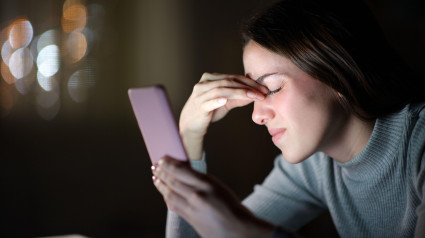 Mujer cansada que sufre fatiga visual al usar el teléfono móvil por la noche en casa