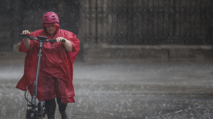 Una mujer circula con su patinete durante las lluvias