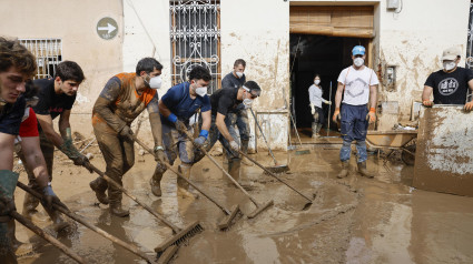 Voluntarios barren el lodo de una calle de Masanasa