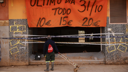 Un hombre mira el interior de un local destrozado que todavía anuncia descuentos este martes en la localidad valenciana de Catarroja