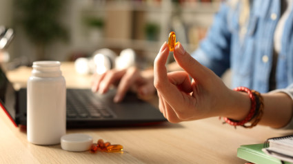 Primer plano de la mano de una estudiante que muestra un estudio que muestra una pastilla de vitaminas por la noche sentada en un escritorio en casa