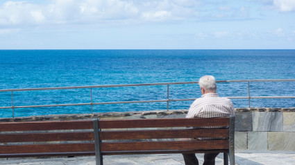 Anciano sentado en un banco mirando al mar en España