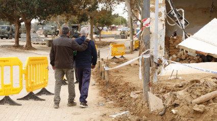 Dos personas caminan junto a una vivienda destrozada por el paso de la dana en Picanya