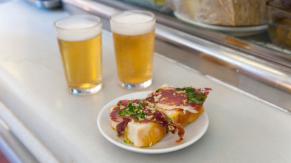 Primer plano de tapas de jamón serrano y cervezas en la barra del bar