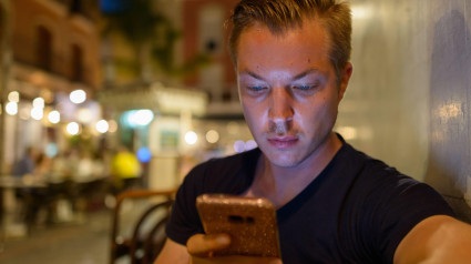 Joven turista guapo usando un teléfono móvil al aire libre