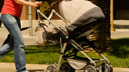 Perfil lateral de una mujer caminando con un cochecito de bebé y sosteniendo un teléfono móvil