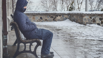 Hombre sentado en un banco en invierno con nieve en el suelo