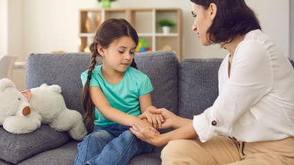 Madre sentada con su hija, tomándole la mano, hablándole y enseñándole algo