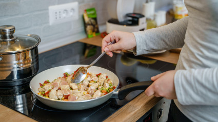 Vista lateral de una mujer caucásica desconocida con una sartén preparando una comida saludable vegana o vegetariana en casa