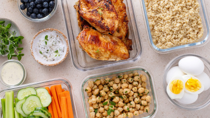 Recipientes de vidrio con quinoa, garbanzos, huevos y verduras frescas listas para preparar comidas.