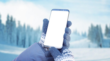 Teléfono inteligente en la mano con guantes. Concepto de uso de un teléfono móvil para planificar una ruta de senderismo. Montaña con nieve de fondo