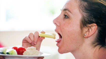 Mujer joven de unos 20 años comiendo comida saludable de pepino con hummus o hummus elaborado con garbanzos cocidos, ajo, especias, tahini, aceite de oliva y