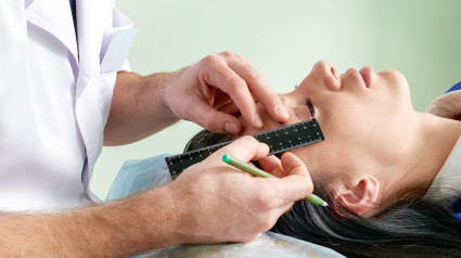 Cirujano plástico y mujer joven con líneas de corrección antes de la cirugía estética, dibujando líneas en los ojos.