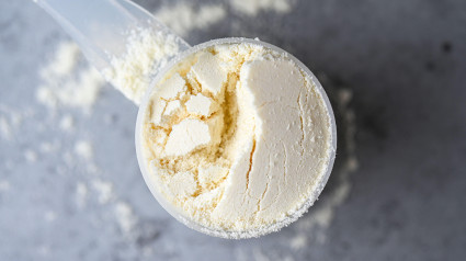 Vista superior de una cucharada de nutrición deportiva, proteínas, creatina y ganador en forma de polvo blanco sobre fondo gris