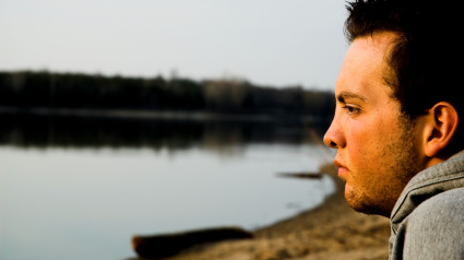 Un joven que parece deprimido en una playa cuando el sol se está poniendo