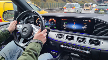 Comodidad y éxito: un hombre conduce un Mercedes GLE híbrido en carreteras urbanas, vista del interior, volante