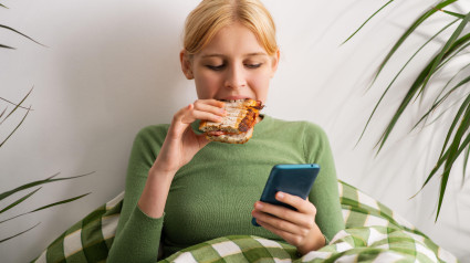 Una niña se deteriora mentalmente, acostada en la cama todo el día, pasando su tiempo en la cama con un teléfono, comiendo tostadas.