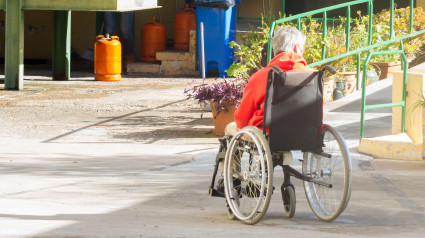 Un anciano solitario en silla de ruedas aprovecha los rayos del sol de la calle para calentarse en invierno