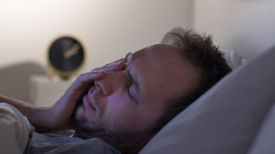 Concepto de insomnio y pesadillas. Un hombre no puede dormir después de una fiesta, se acuesta en la cama por la noche y tiene el despertador sobre la mesilla de noche. Trastornos del ciclo sueño/vigilia