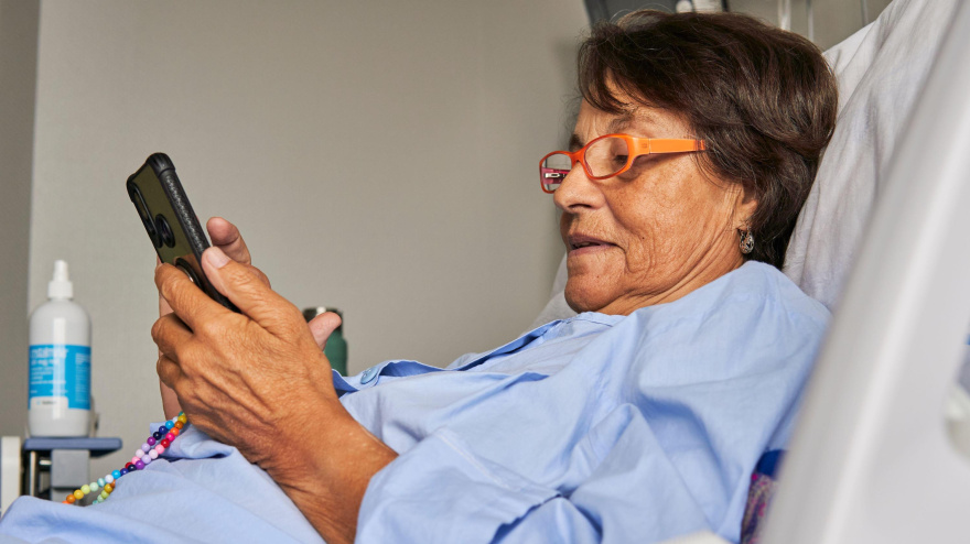 Una señora tumbada en una camilla de hospital mira su teléfono móvil