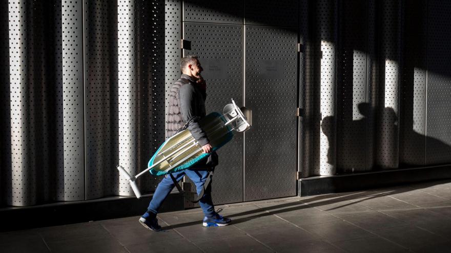 Un hombre carga con una tabla de planchar por la calle