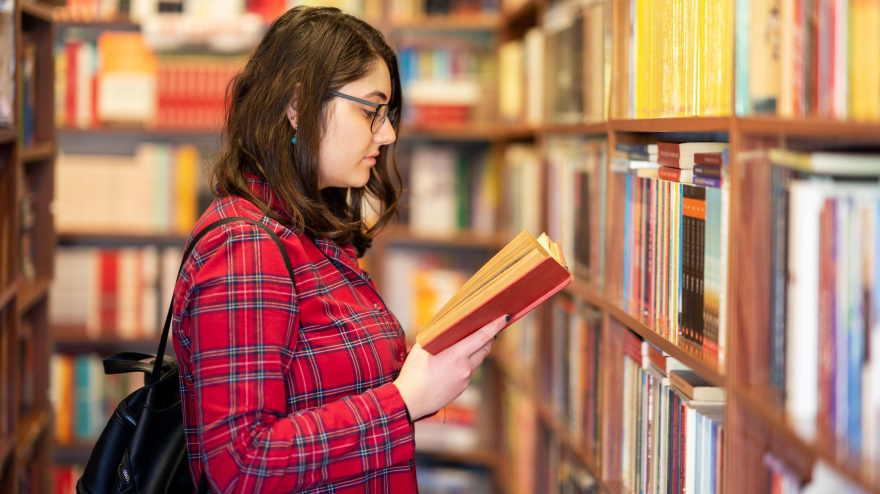 Una chica adolescente sosteniendo un libro en una biblioteca