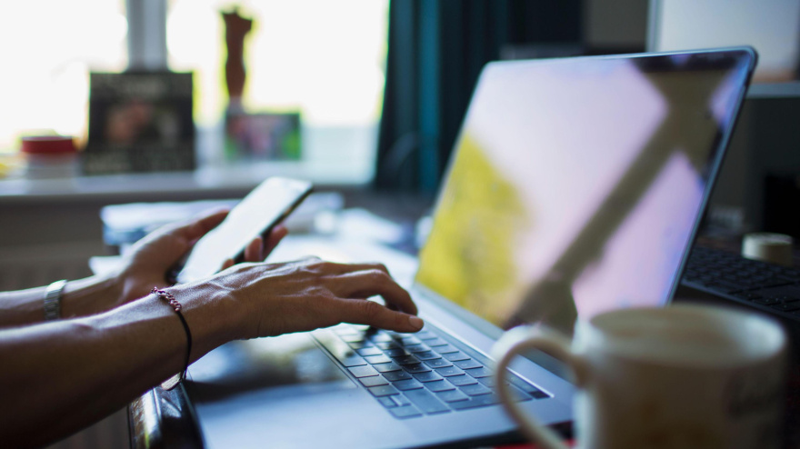Una mujer teletrabajando desde casa con un ordenador portátil y un teléfono móvil