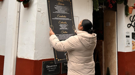 Una empleada instala los paneles informativos en la fachada de un establecimiento en la Judería.