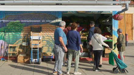 Un puesto de venta de verduras de agricultores locales, con compradores haciendo fila al aire libre