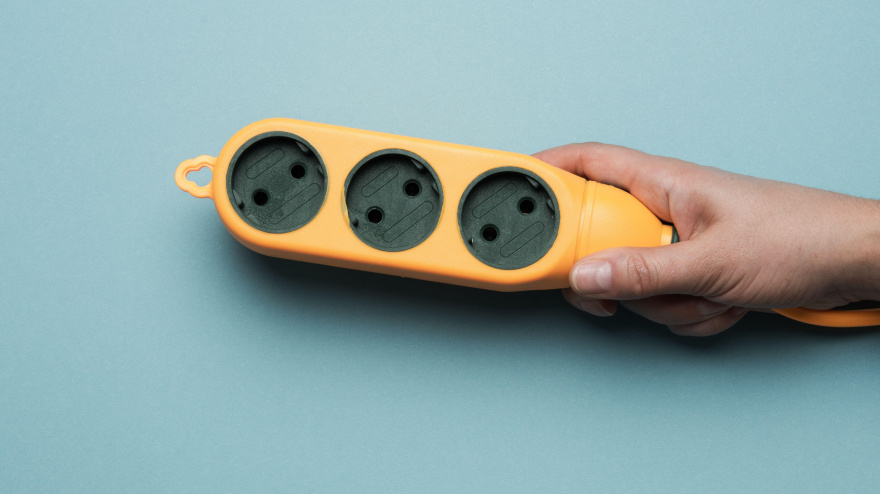 Regleta de enchufes de goma de color naranja con tres enchufes sobre fondo azul