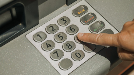 Dedo de una mujer presionando una tecla en el teclado de un cajero automático callejero en un día soleado en Mérida