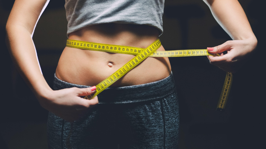 2WRG9CB Slim girl bodybuilder centimeter measuring her waist in a gym. Sports concept, fat burning and a healthy lifestyle.